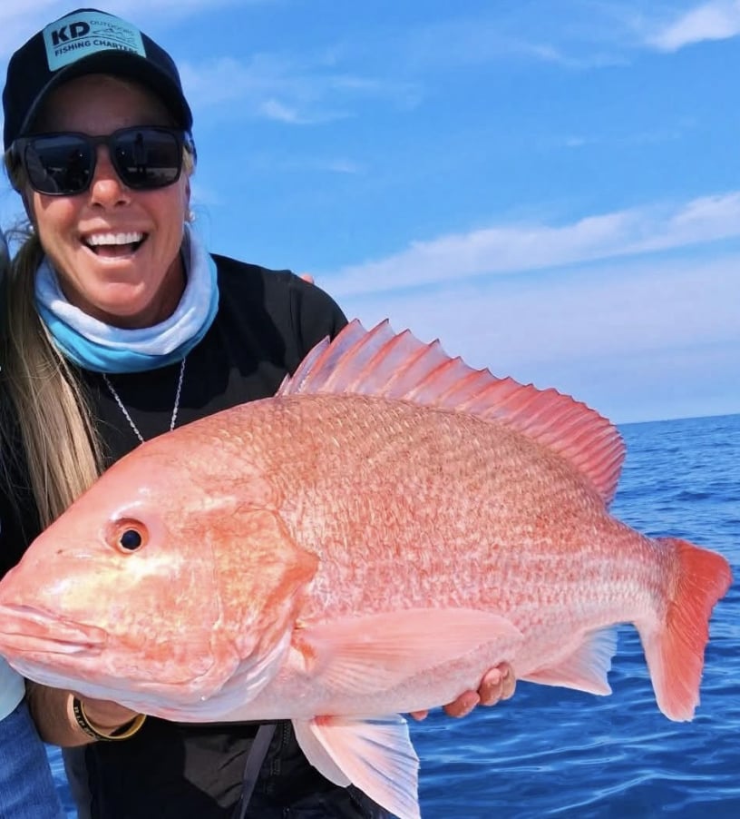 Woman wearing a hat smiling  on the water hold a red snapper fish